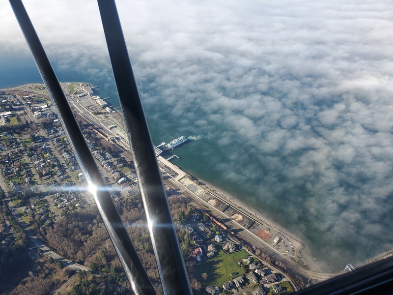 Photo of a ferry boat at dock
from above, showing the coastline, and a feathery layer of clouds
fading into solidity behind the ferry